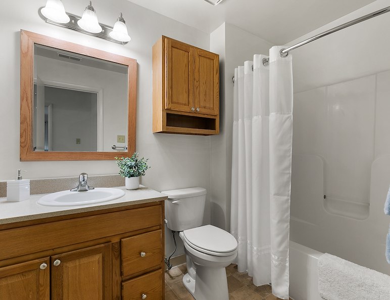 Bathroom in California Furnished Apartments, featuring wood cabinets, a mirror, and a shower curtain, offers modern comfort