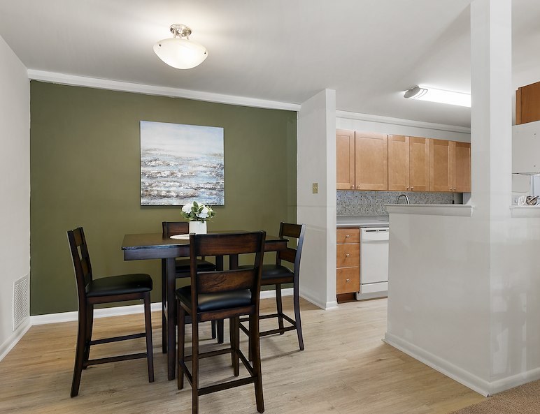 Dining area in California Furnished Apartments features a dark wood table, green accent wall, and open kitchen with light cabinets
