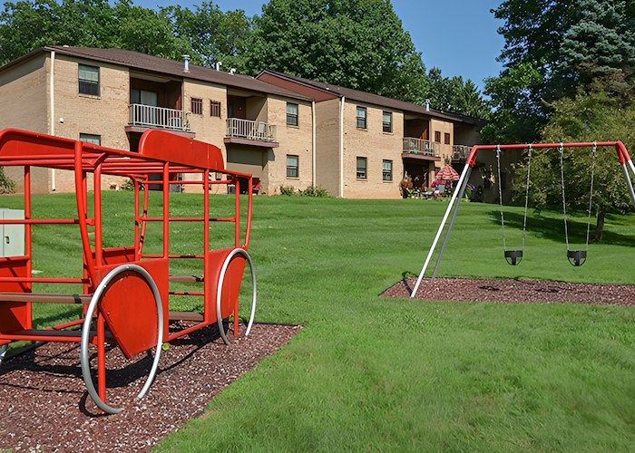 A red wagon and swings are in front of an apartment complex, Powder Mill Apartments, York, Pennsylvania
