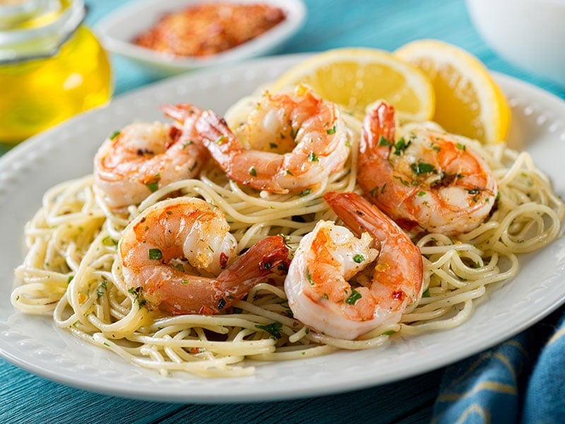 A plate of shrimp scampi with linguine and lemon slices.