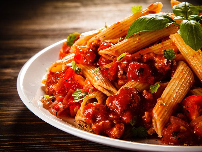 A plate of pasta with tomato sauce and basil leaves on a wooden table.
