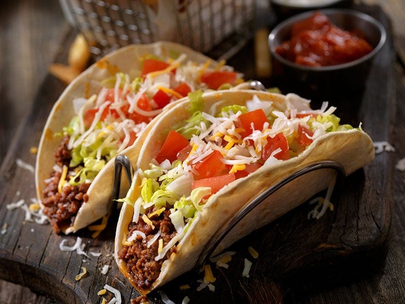 Three tacos on a wooden board with a bowl of salsa