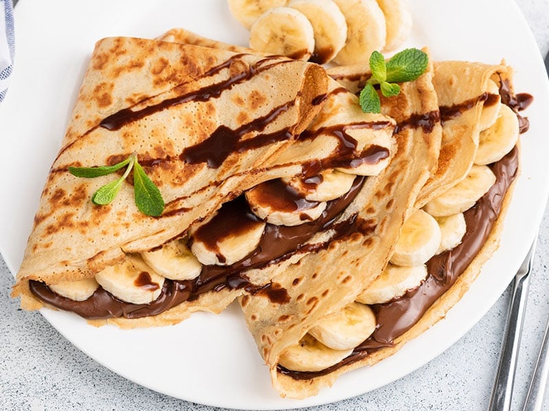 A plate of crepes filled with bananas and chocolate sauce, garnished with mint leaves.