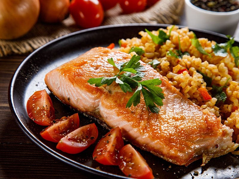 A plate of food with a piece of salmon, rice, and tomatoes.
