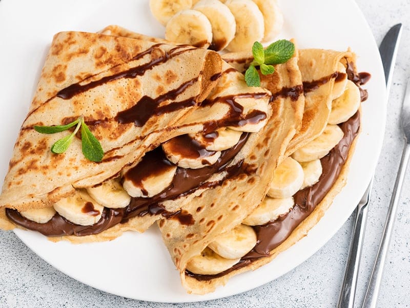 A plate of crepes filled with bananas and chocolate sauce, garnished with mint leaves.