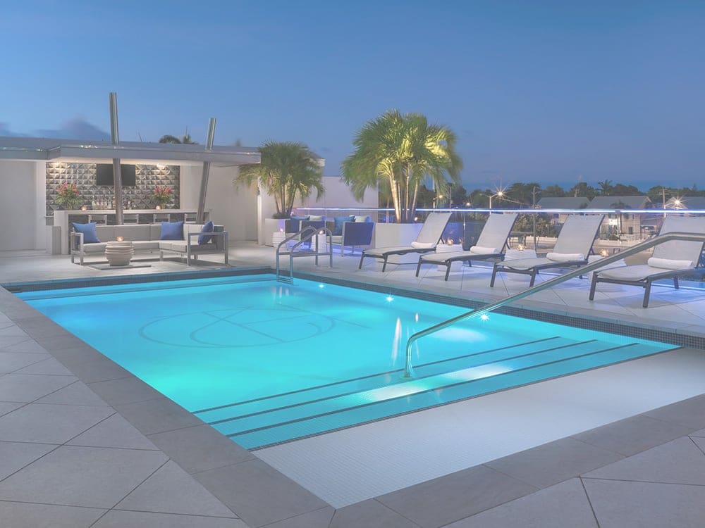 A nighttime view of a rooftop pool with lounge chairs and a bar area.