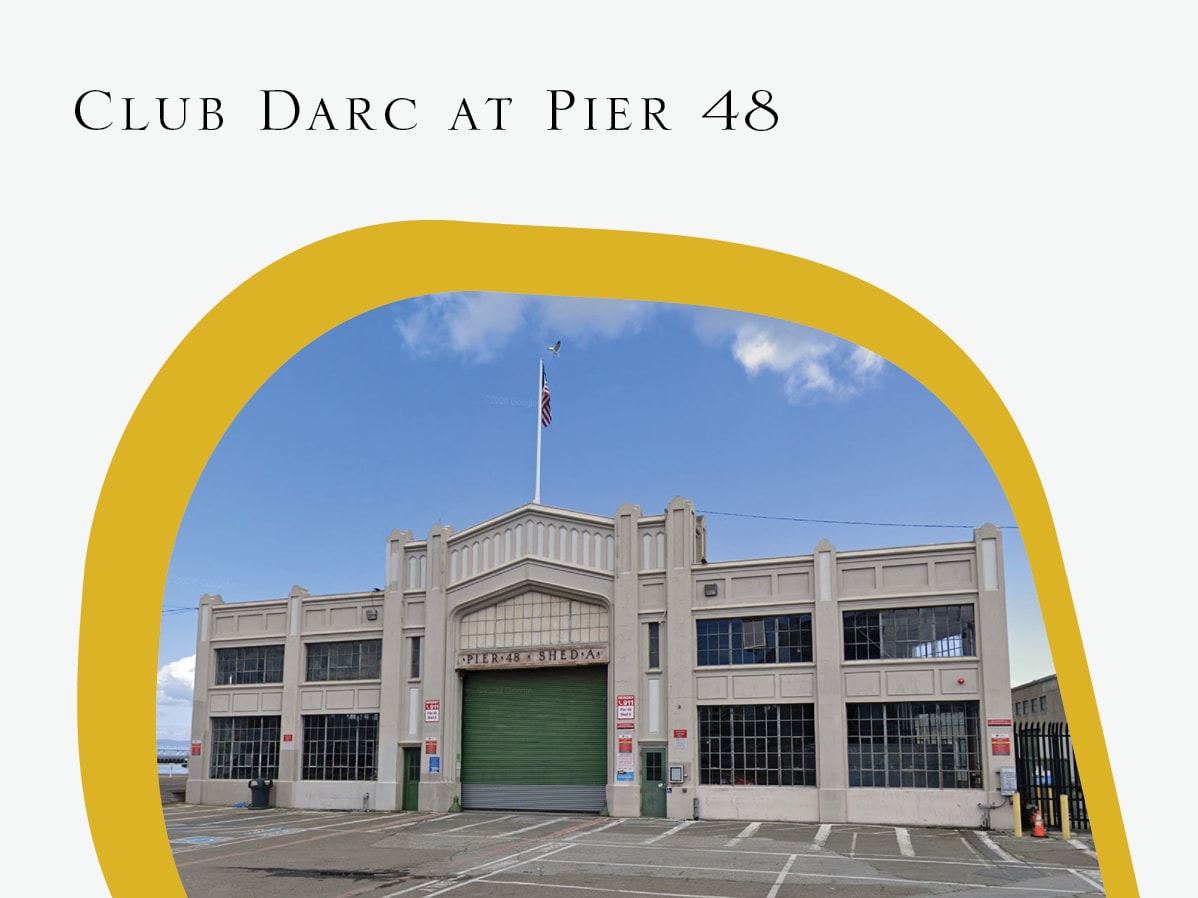 A large gray building with a green garage door and a flagpole in front of a blue sky.