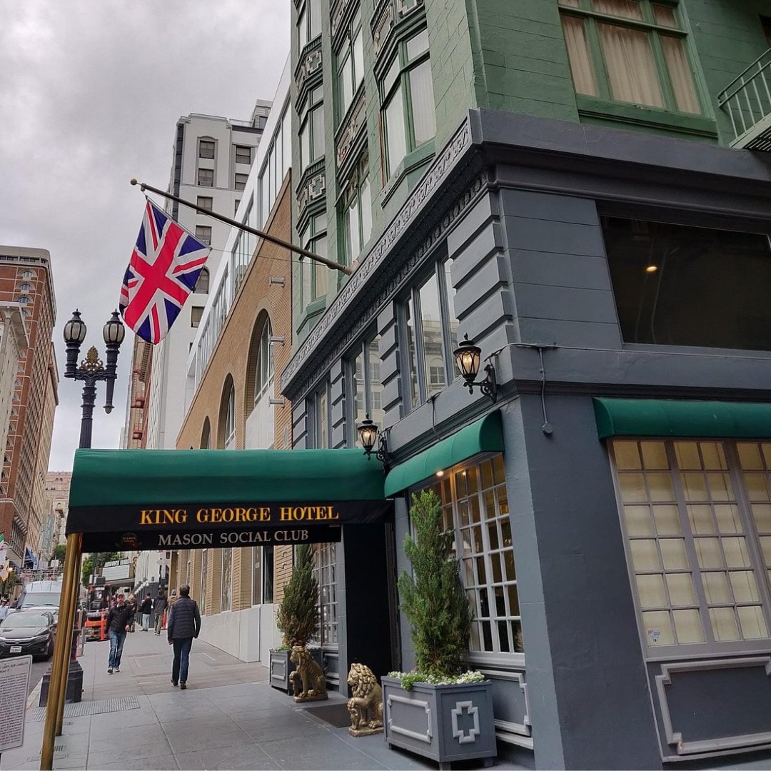 The exterior of the King George Hotel with a green awning and gold lettering, a British flag flying above.