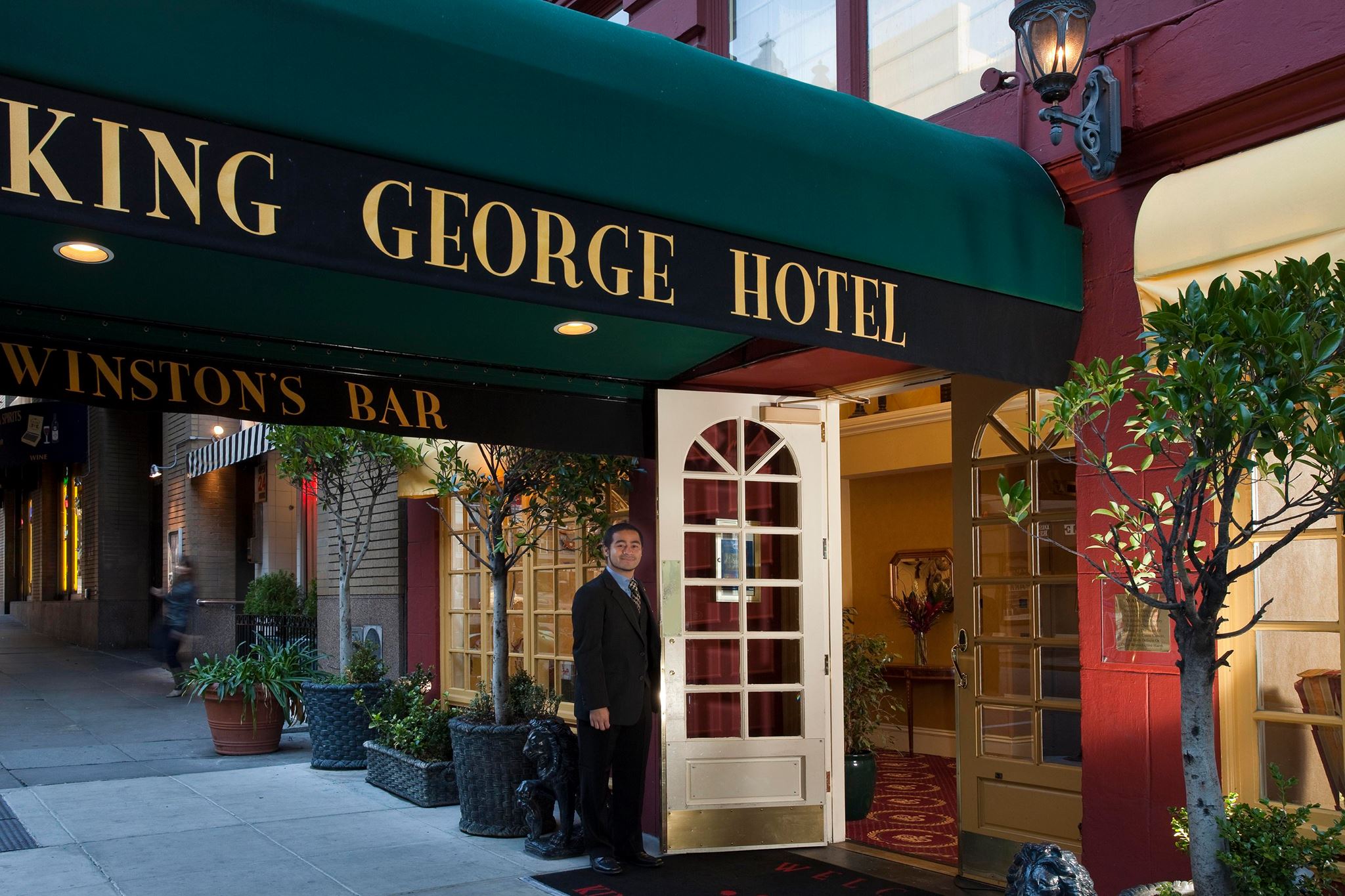 The main entrance of the King George Hotel with a green awning and a man standing in the doorway.