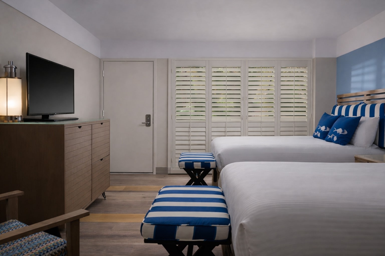 A hotel room with two beds, two benches, and a window with shutters.