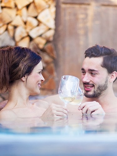 A man and woman in a hot tub with wine glasses