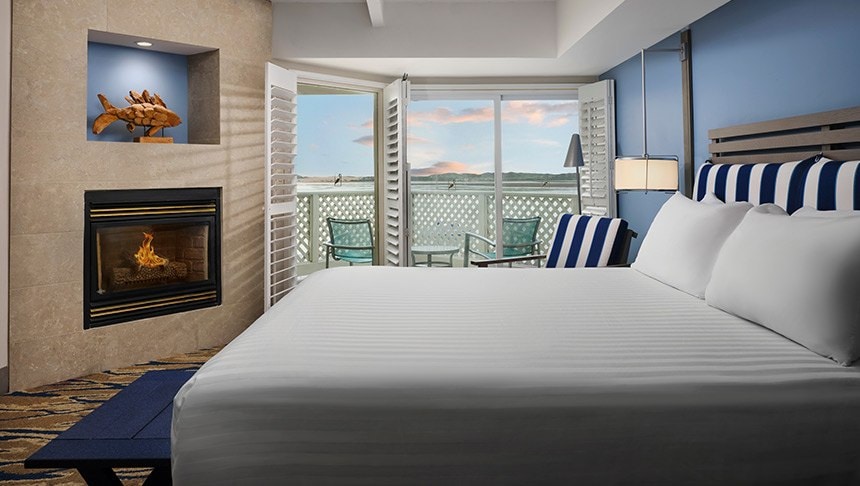A hotel room with a large bed, fireplace, and balcony with a view.