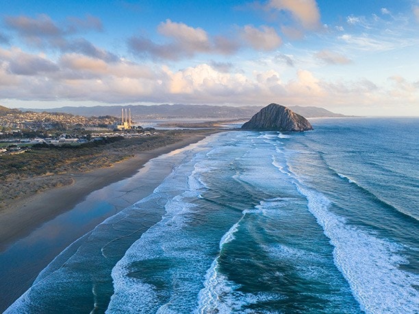Aerial view of a beach with waves and a rock formation in the distance.