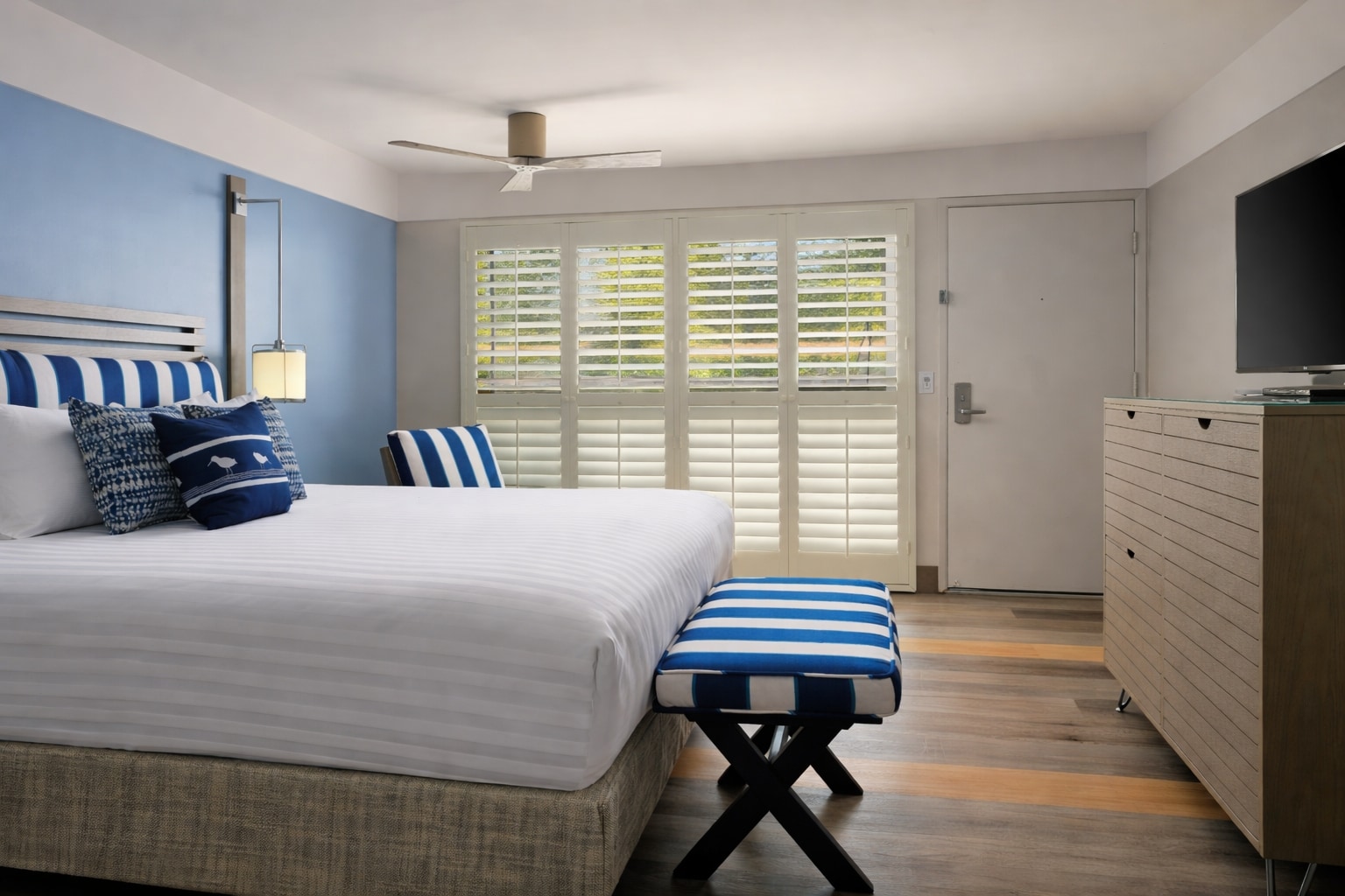 A hotel room with a bed, dresser, and window with shutters