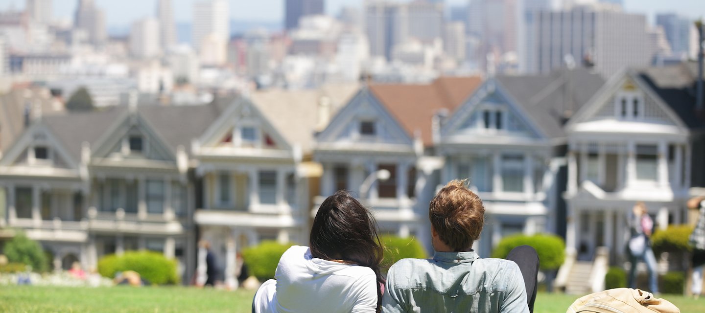 A couple lounging on a grassy hill overlooking the Painted Ladies landmark in San Francisco