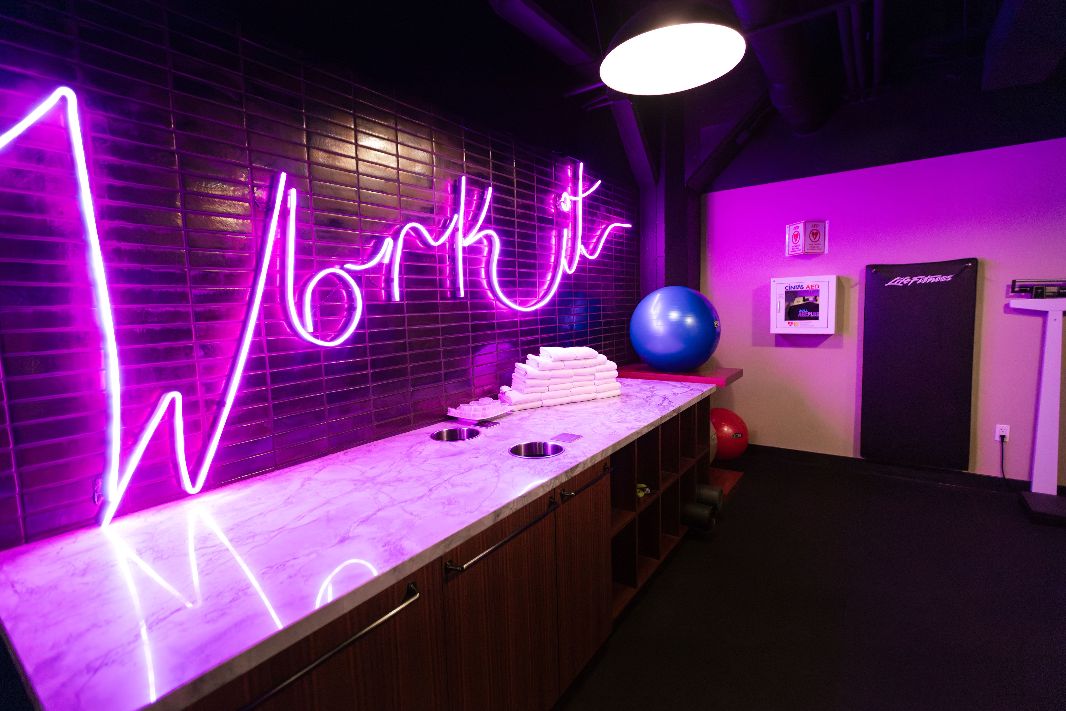 A gym counter with a neon 'Work it' sign, marble countertop, exercise balls, and towels.