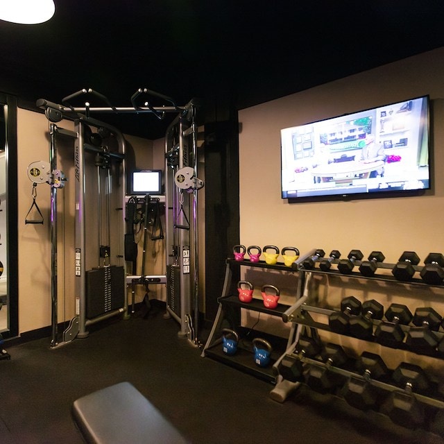 A gym with various exercise equipment including dumbbells, kettlebells, and a TV on the wall.