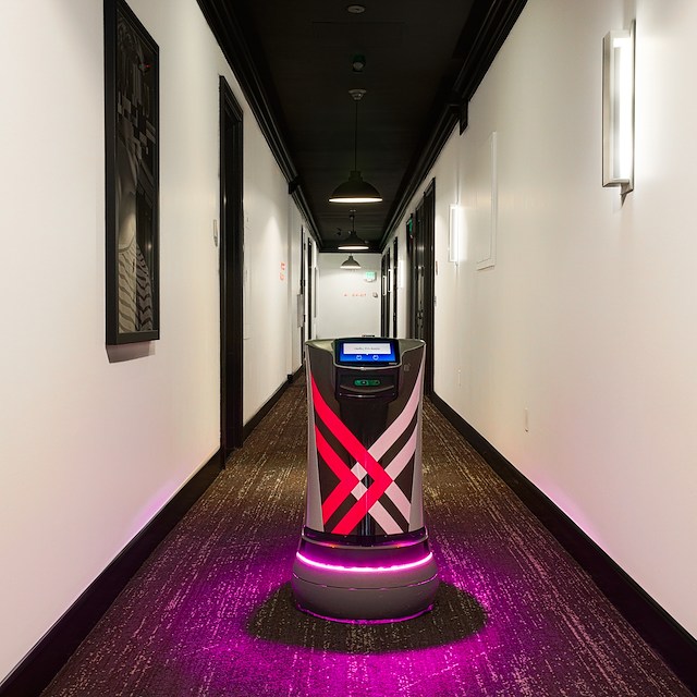 A robot stands in a hotel hallway with doors and lights.