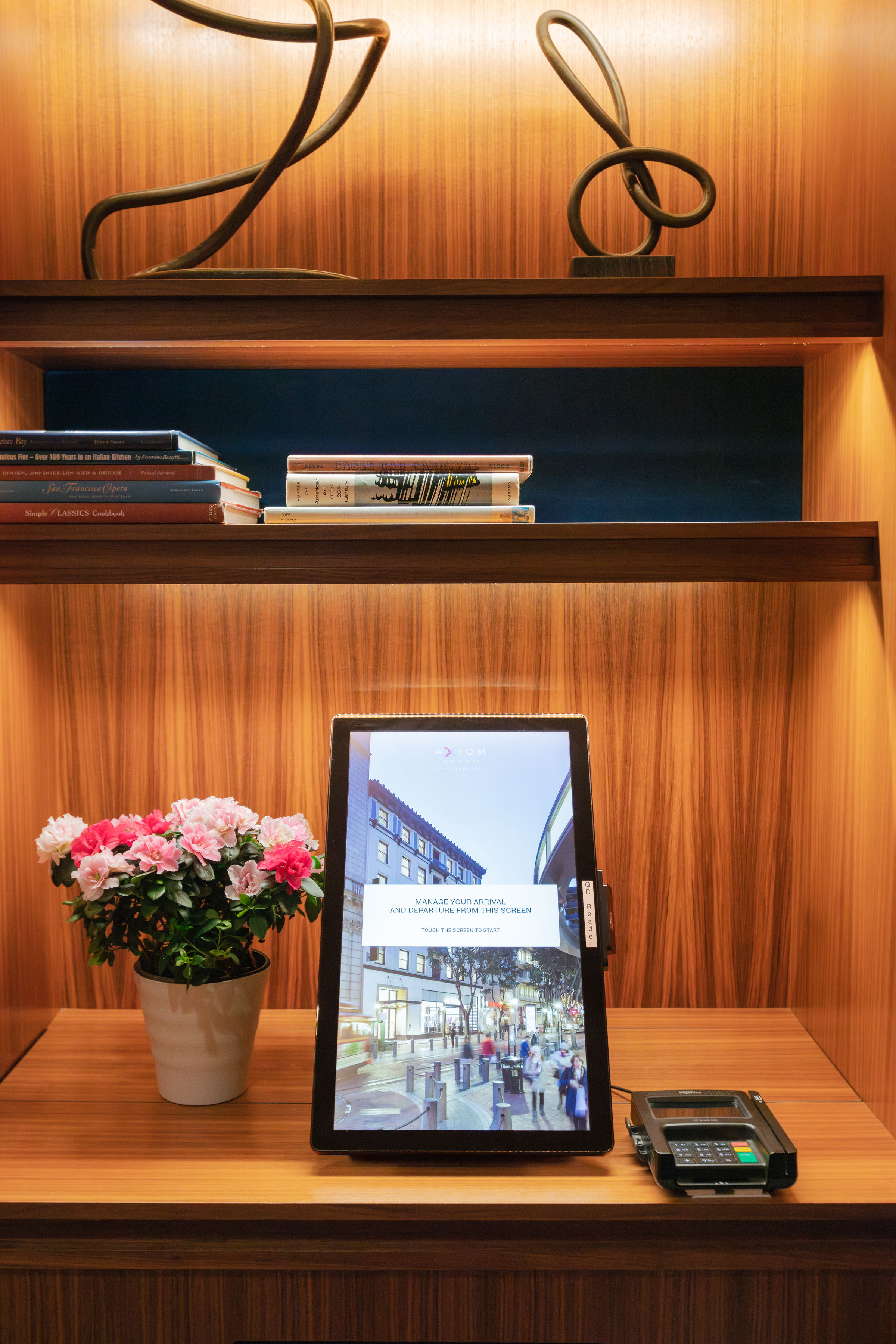 A wooden shelf with a tablet, flowers, and books on it.