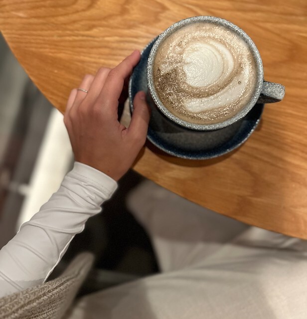 A hand holding a coffee cup on a saucer over a wooden table.