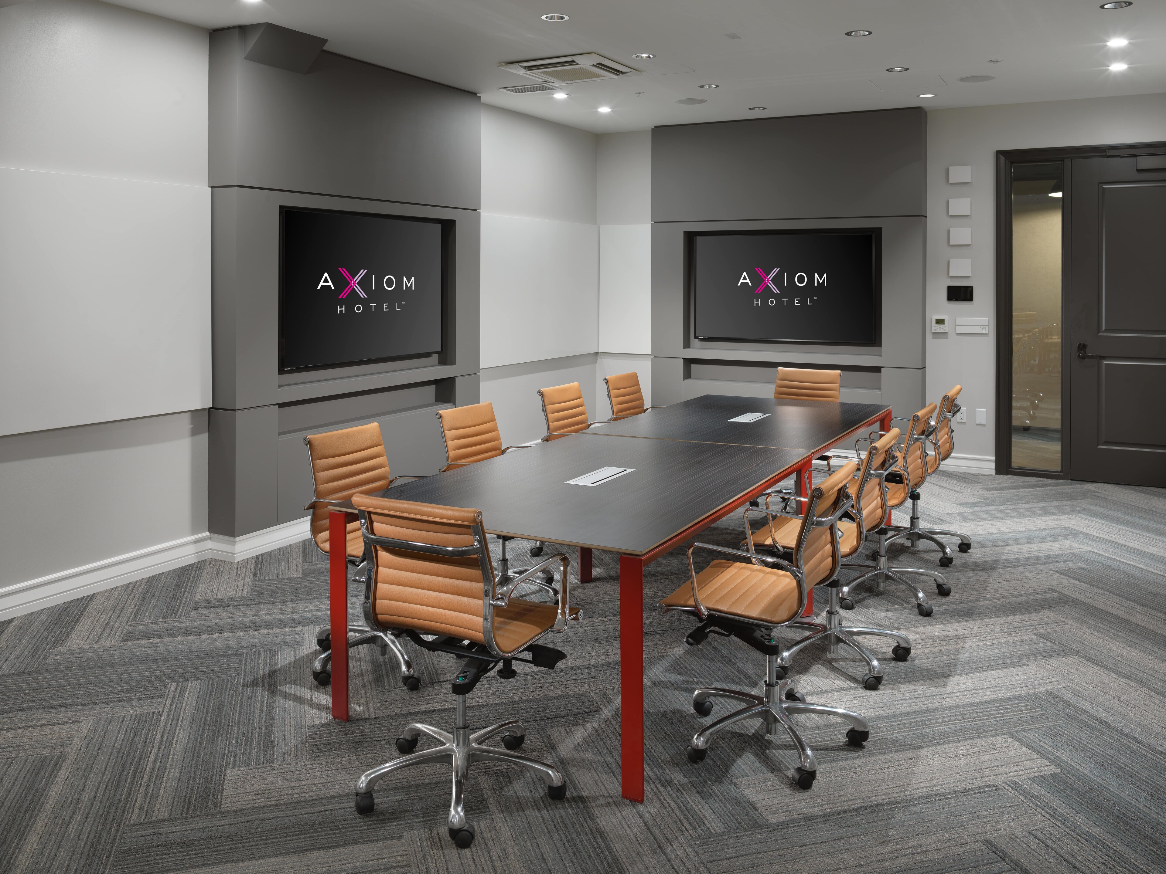 A modern conference room with a long table, brown chairs, and two screens at The Axiom Hotel, San Francisco, California