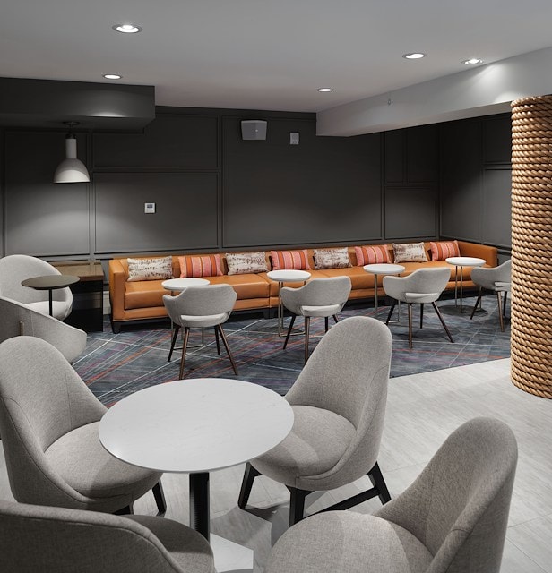 A modern lounge area with a long orange sofa, gray chairs, and small tables.