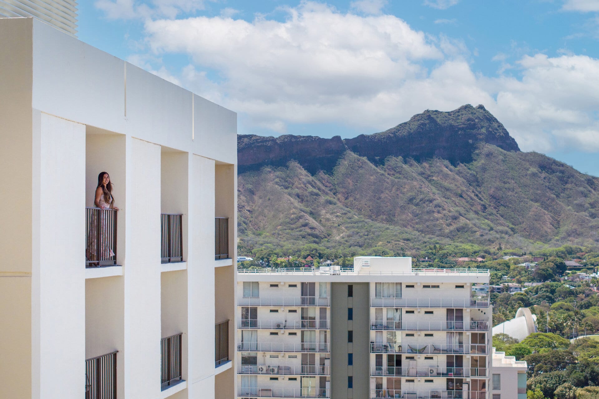a woman standing on a balcony with mountains in the background at our Waikiki hotel