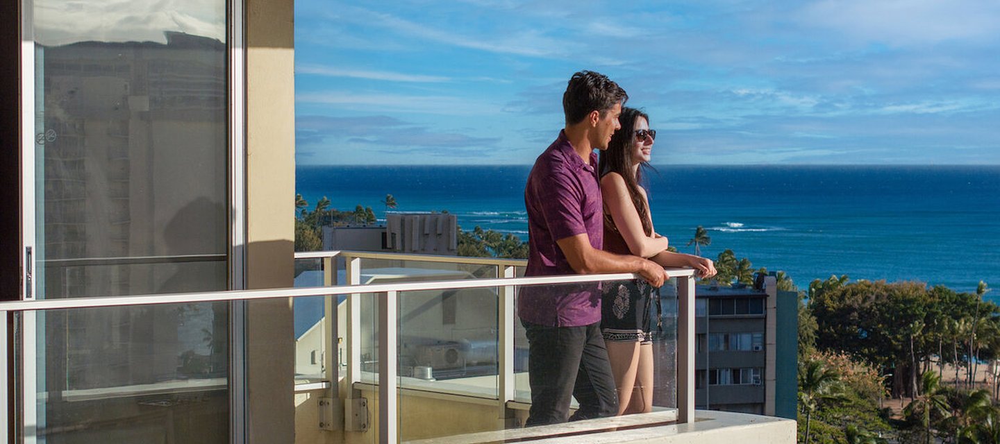 a woman standing on a balcony with mountains in the background at our Waikiki hotel