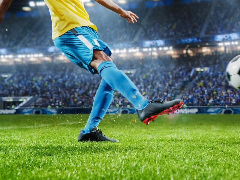 A professional soccer player kicks a soccer ball in a crowded stadium at night