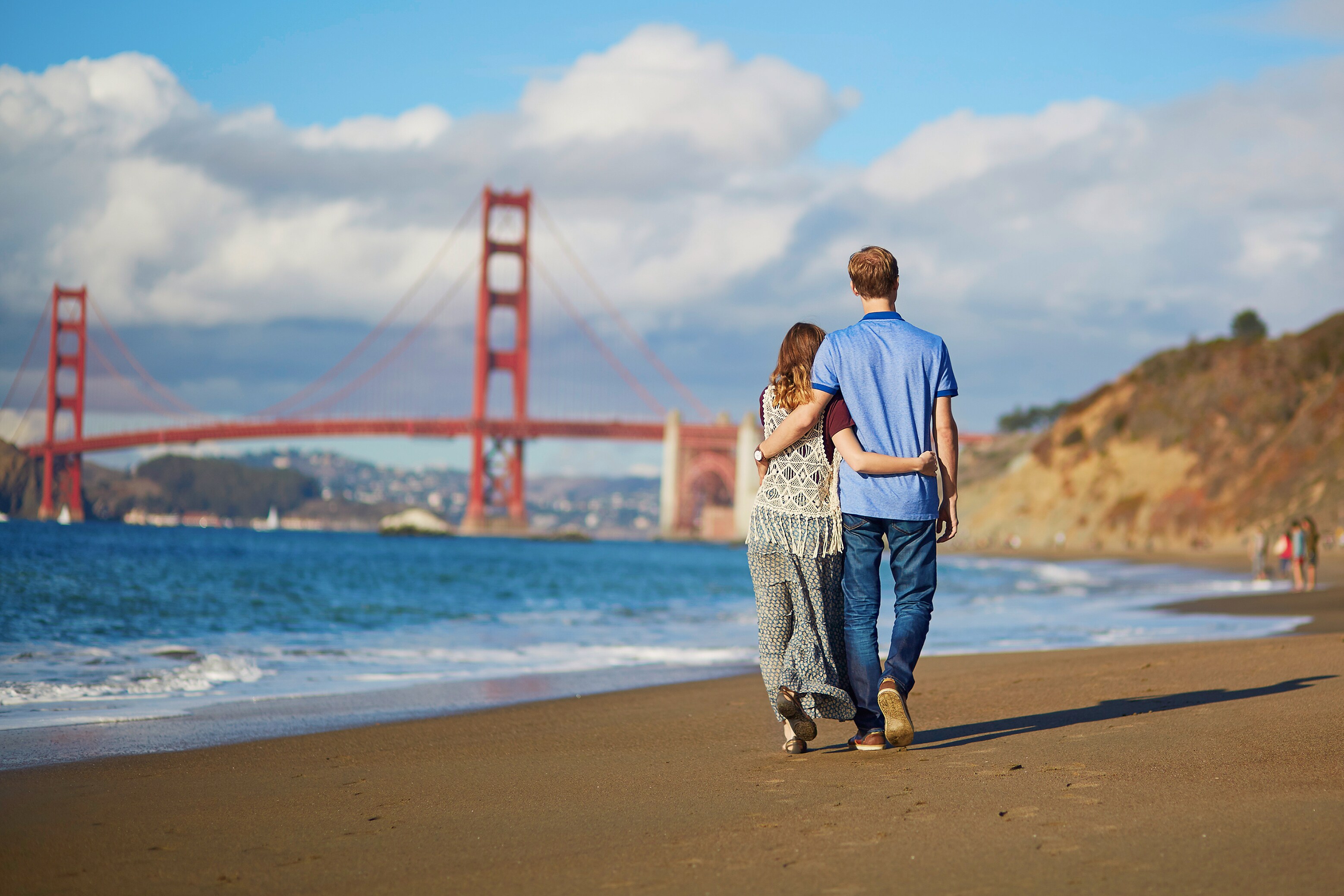 A couple enjoys a beach walk near The Axiom Hotel in San Francisco, California.
