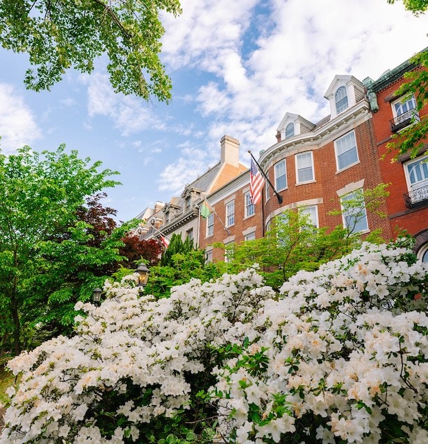 A red brick building with white flowers and green trees in front of it, with an American flag hanging from a pole.