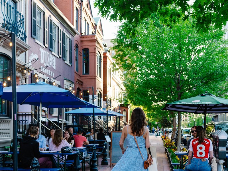 A woman walking down a sidewalk with tables and umbrellas