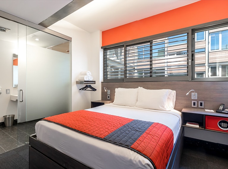 A hotel room with a bed, window, shower, and desk.