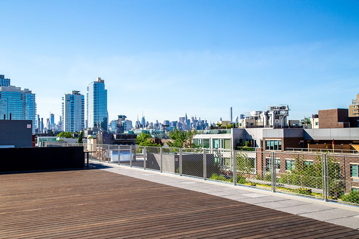 A rooftop deck with a fenced perimeter and a view of the city skyline.