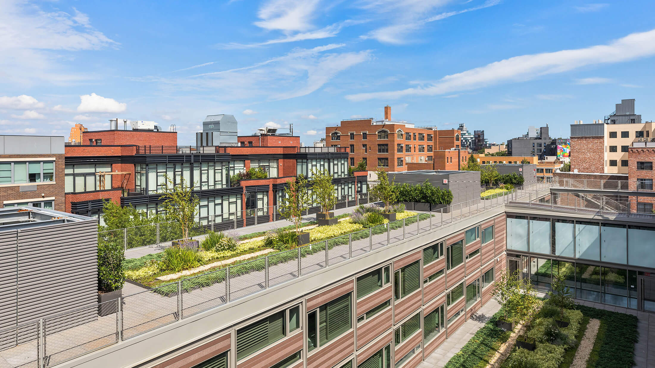 A rooftop garden with a green roof and city view under a blue sky with clouds.
