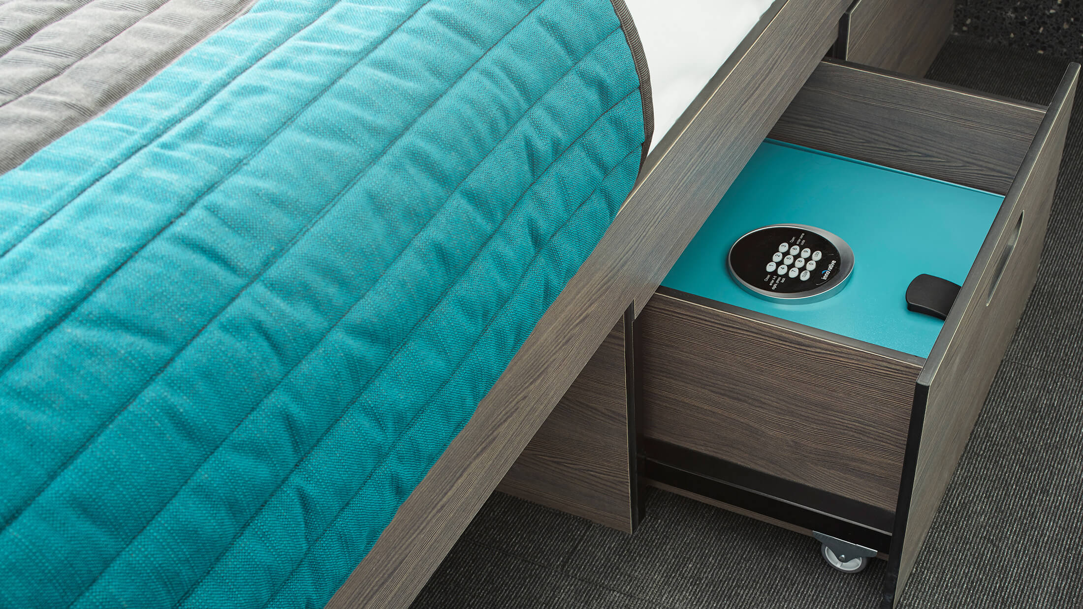 a close-up of a bed with a teal comforter and a safe in a cabinet next to it