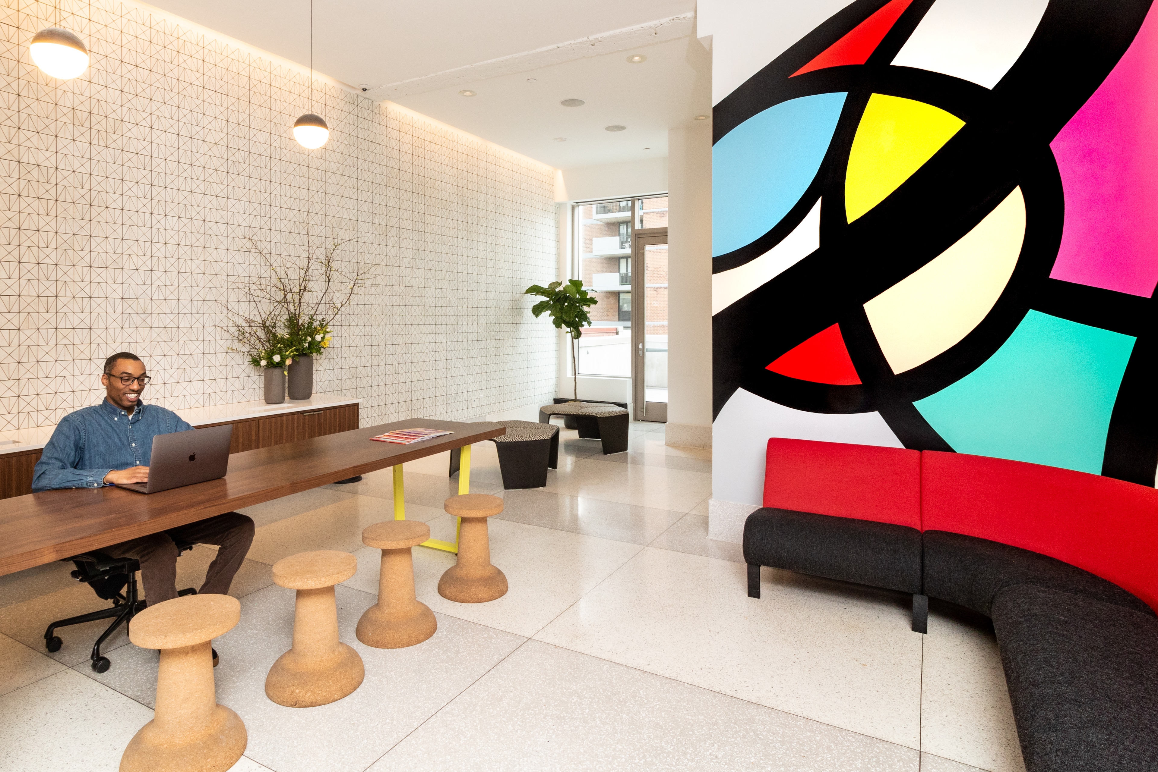 A lobby with a man sitting at a table, a colorful couch, and a large abstract art piece on the wall.