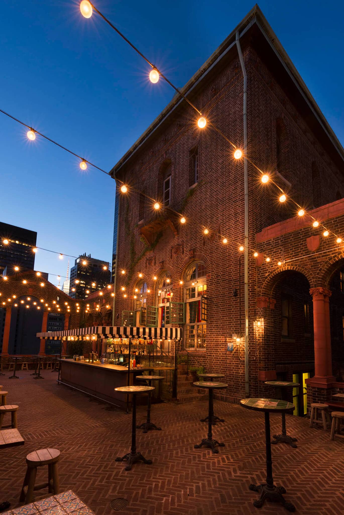 A brick building with a bar and outdoor seating area, decorated with string lights.