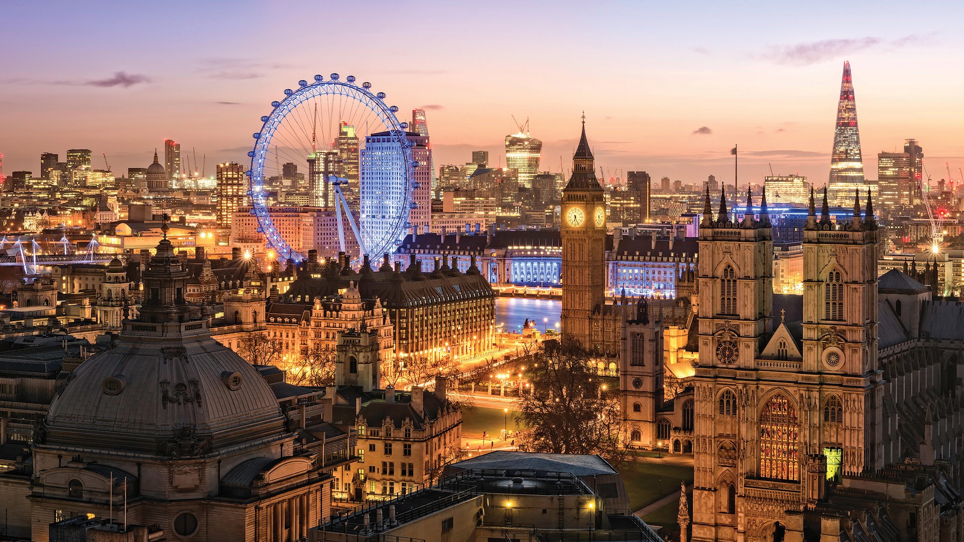 The London Eye towers above the city that’s lit up at night.