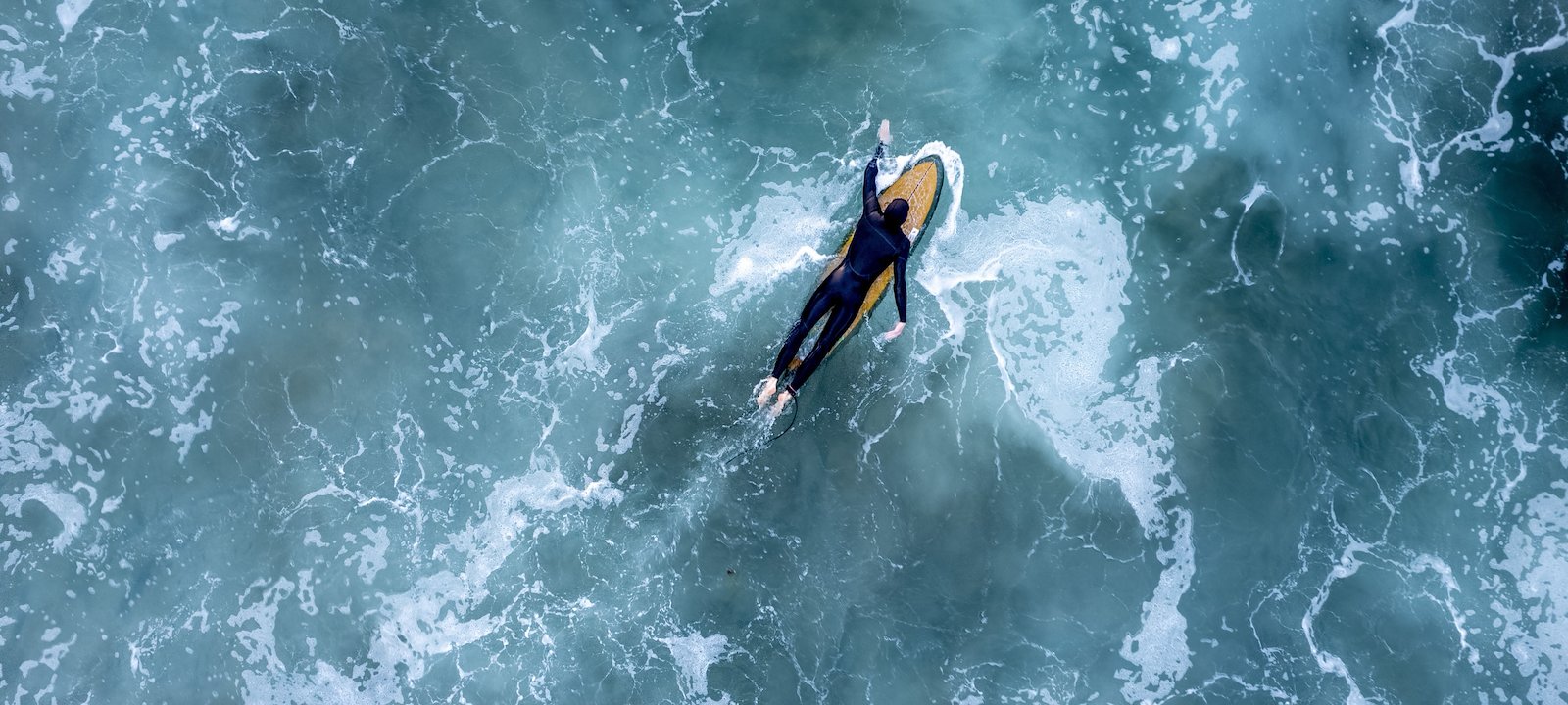 Aerial shot of a surfer paddling out in Newport Beach, California.