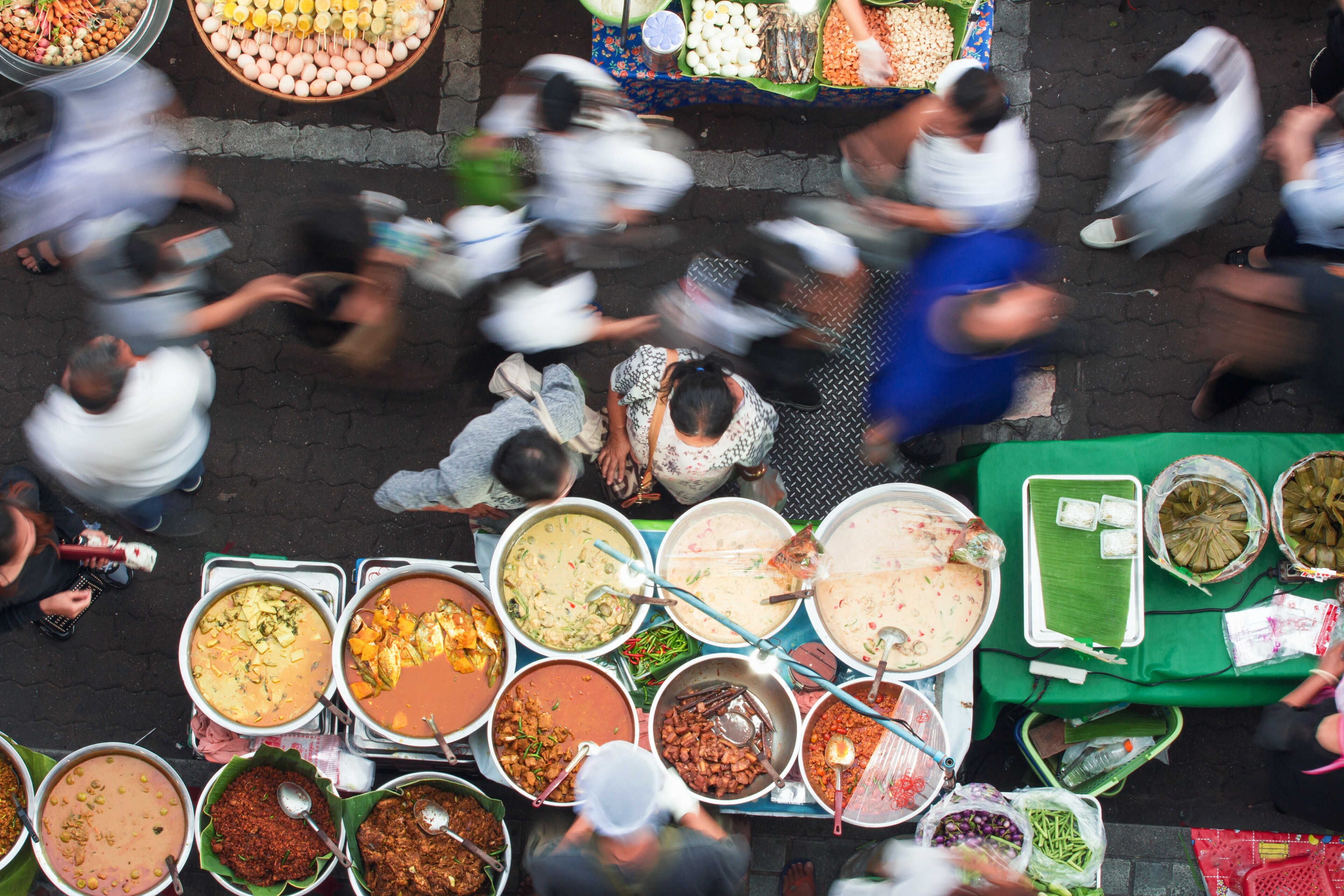 Overhead view of a vendor in Bangkok selling various Thai dishes to the bustling crowd.