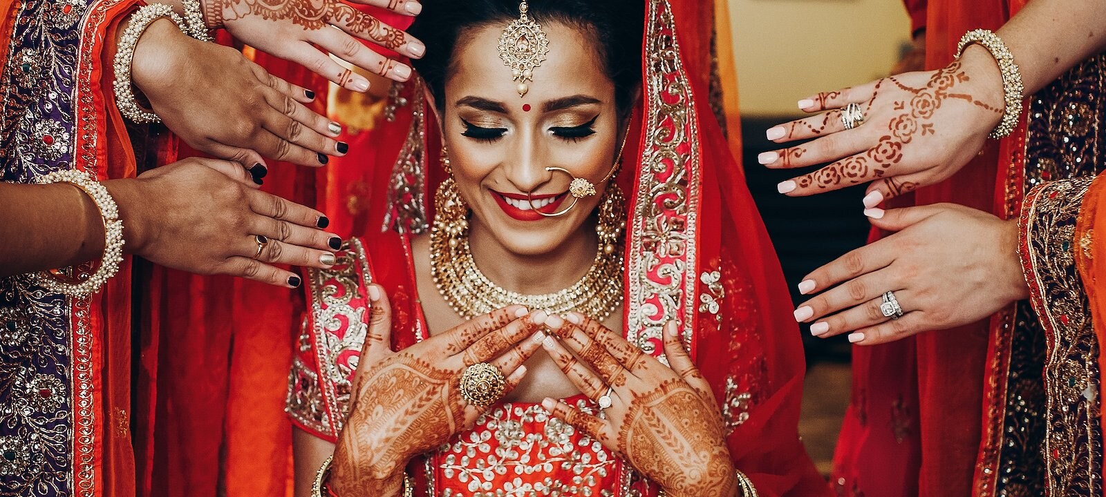 An Indian bride dressed in full traditional Hindu lehenga wedding attire, surrounded by her bridesmaids.