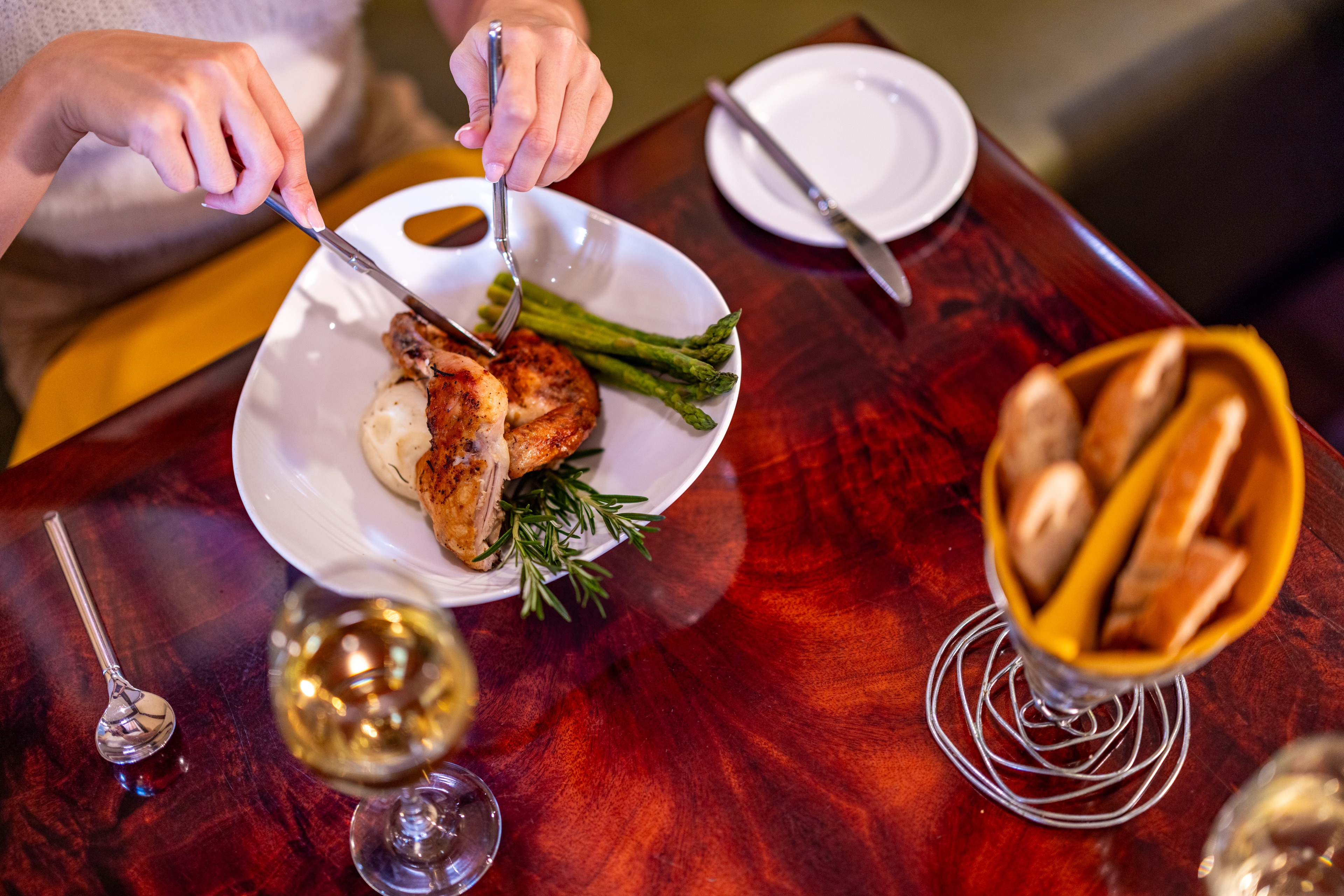 A plated meal with meat, vegetables, and herbs on a white plate, accompanied by a glass of wine and bread.