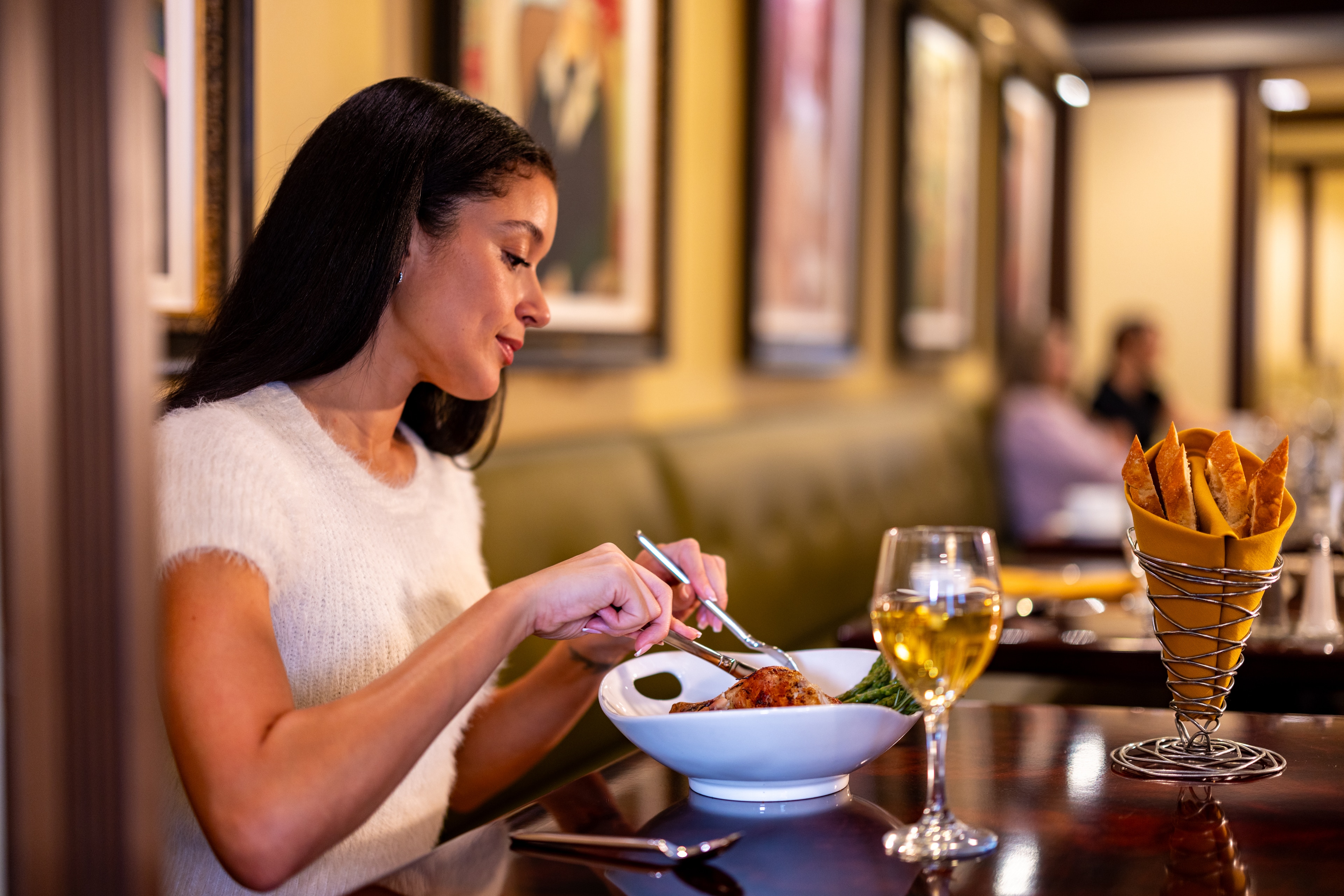 A woman enjoys a meal in a restaurant with a glass of wine and a plate of food.