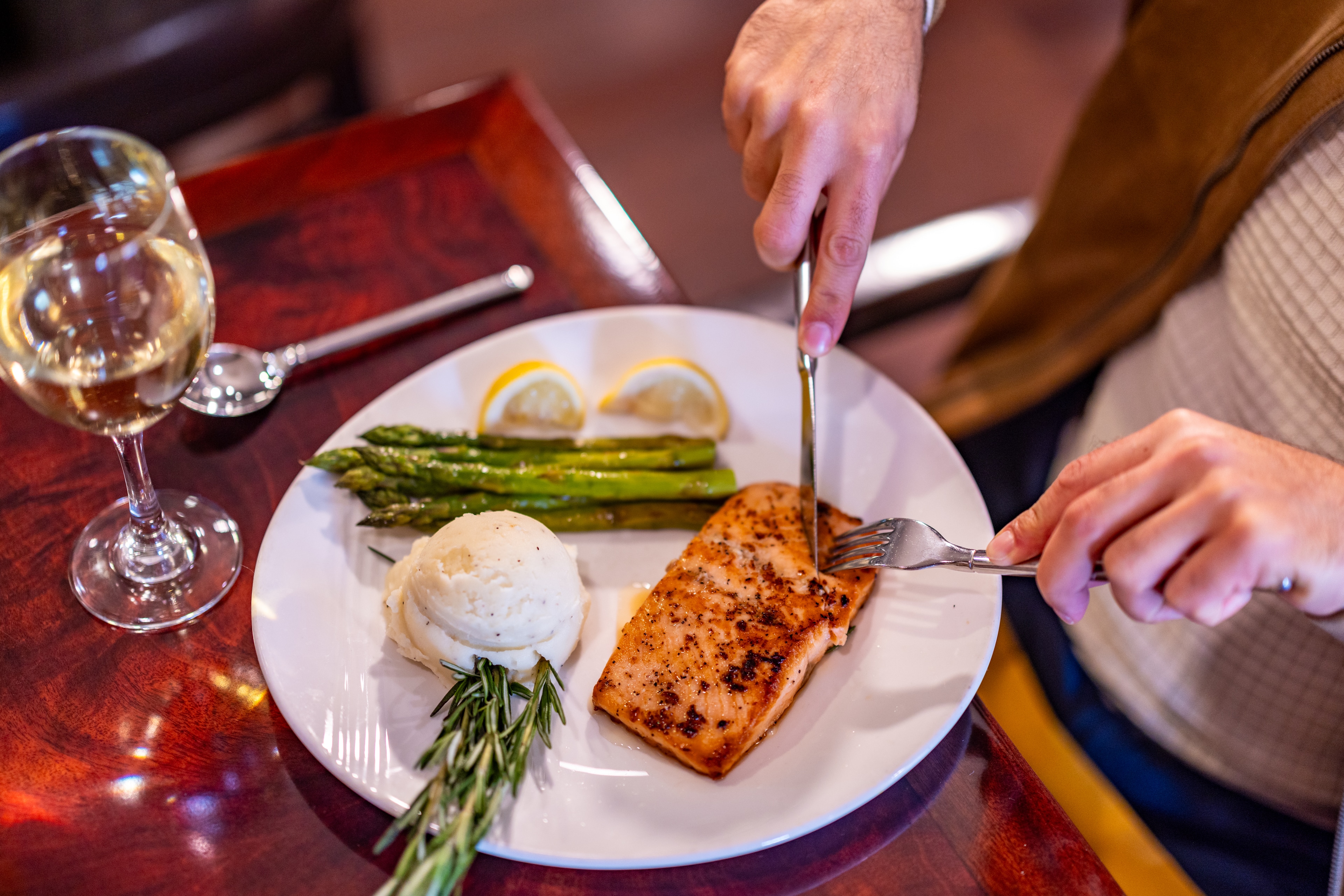 A plated dish of grilled salmon, asparagus, and mashed potatoes with a glass of white wine.