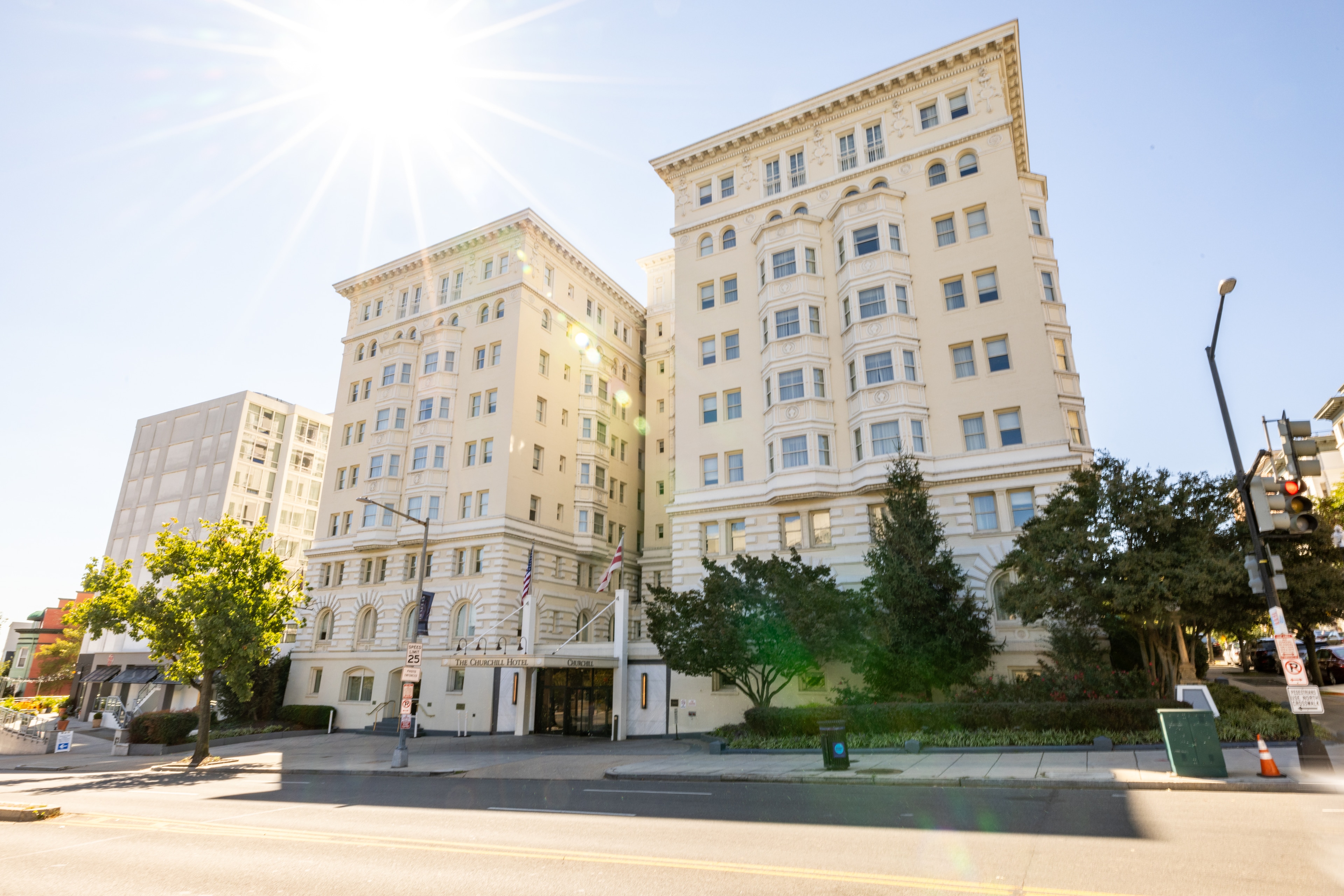 A wide-angle view of a multi-story beige building with trees and a street in front of it.
