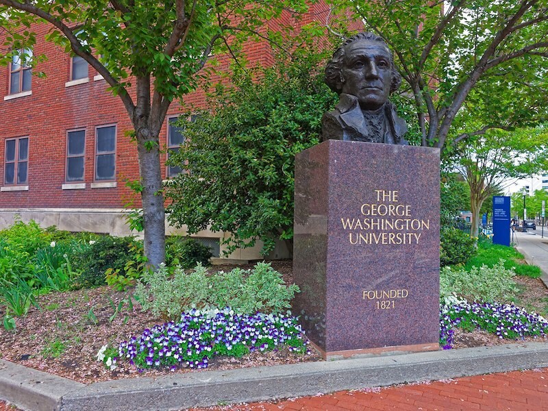 George Washington University statue and sign with lush greenery and flowers on a historic campus pathway