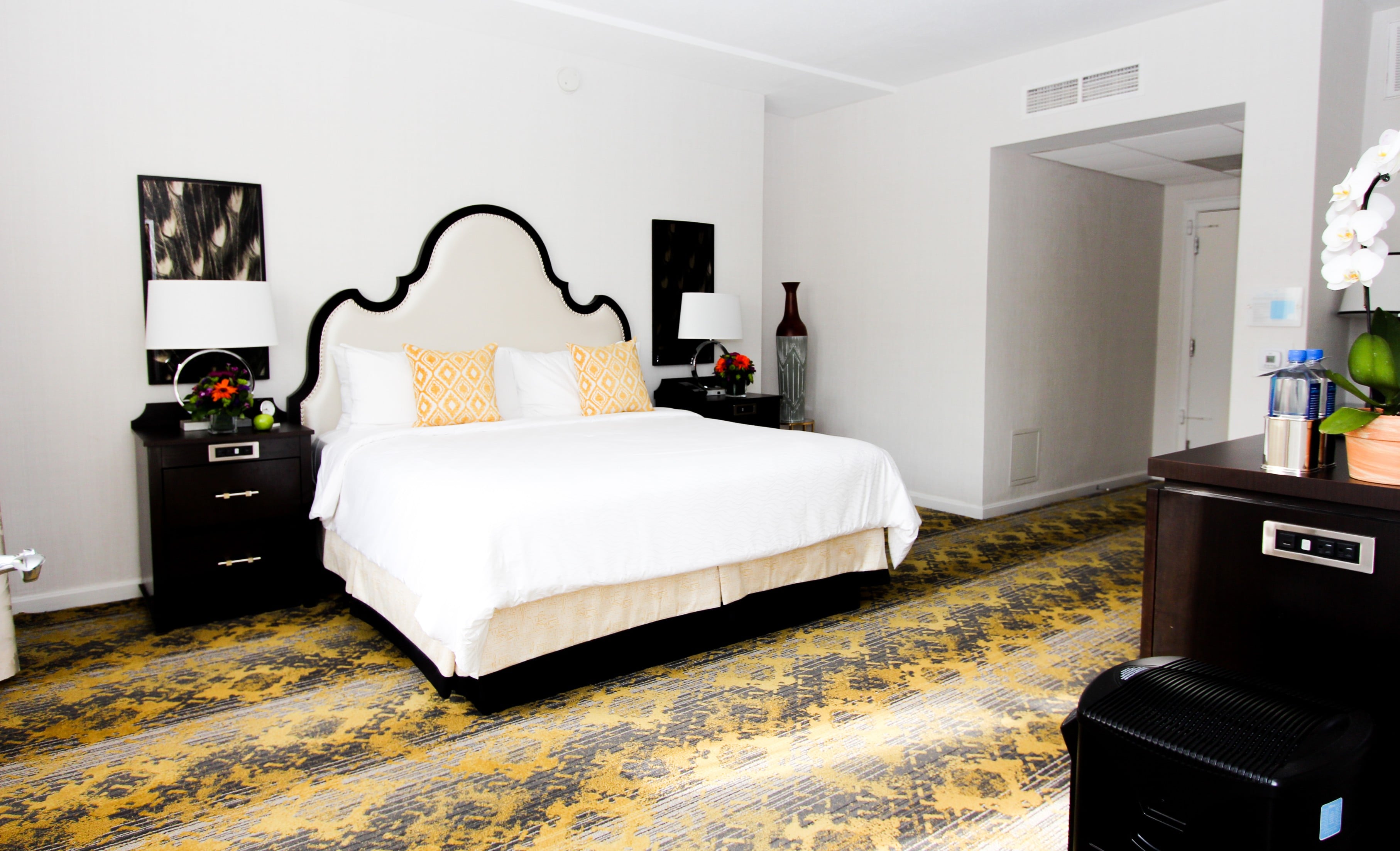 A hotel room with a large bed, nightstands, and a doorway to another room