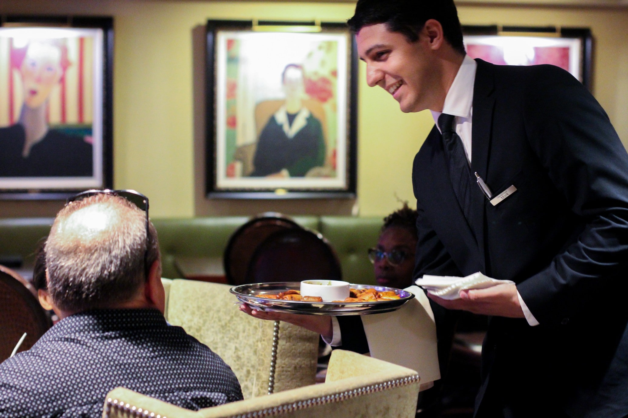 A man in a suit serving food to another man at a table.
