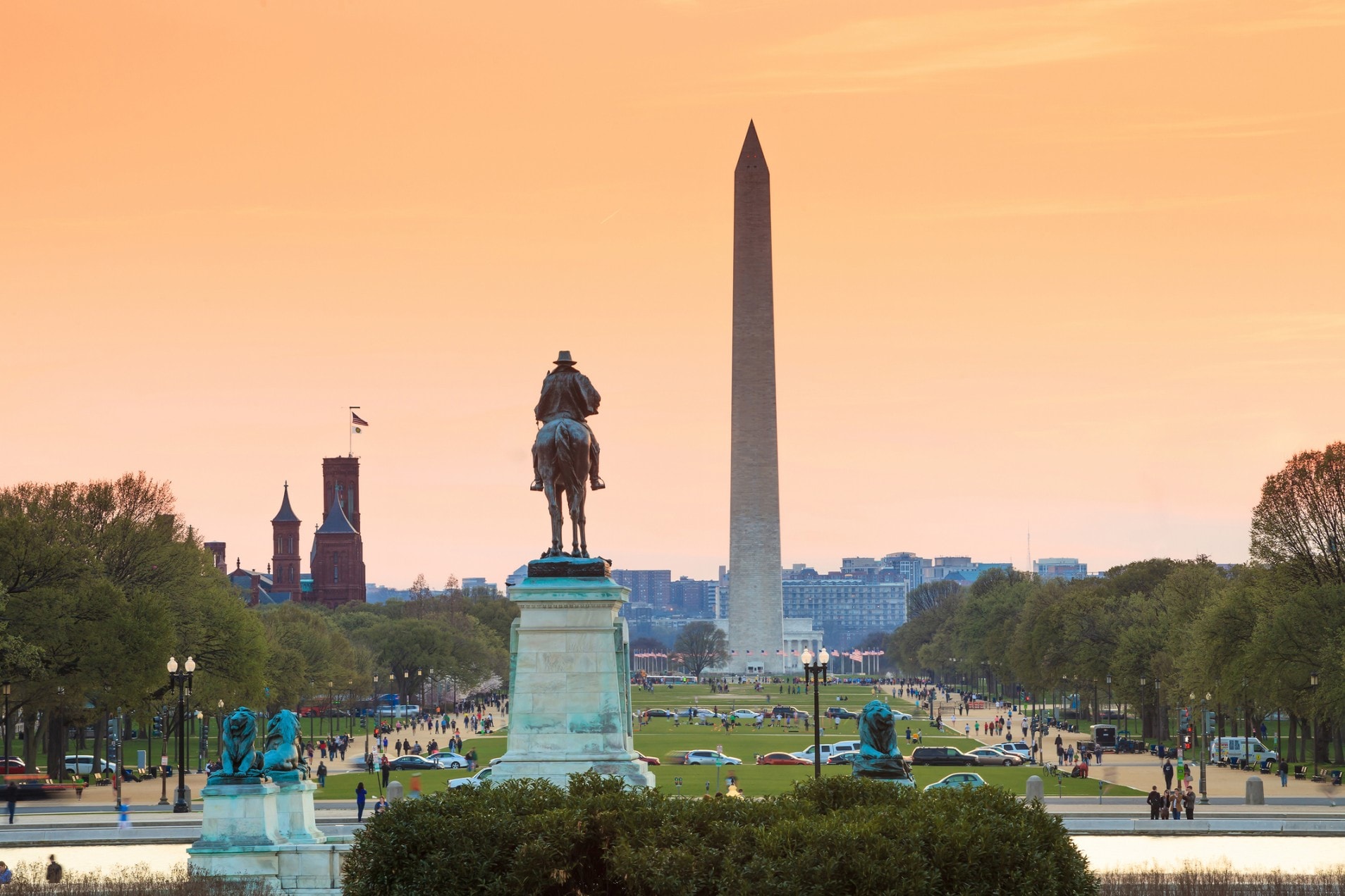 A wide view of the Washington Monument and a statue in a park at sunset.